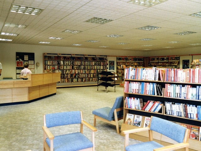 Inside Swinnow Branch Library on Swinnow Lane, taken around the time of its opening in 1987. The counter area is on the right, while in the foreground on the left are large print books, with easy chairs around.