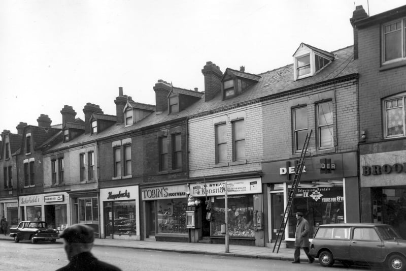 Shops and businesses on Kirkstall Road in March 1966. Businesses in view are Schofields drapers, Doreen Hammonds hair fashions, William Pound, butchers, Hagenbachs continental bakery, Tobins footwear, Walter Stead, tobacconists toy shop and small lending library and DER television rentals. On the right edge part of a branch of Brooke Bros. menswear can be seen, this shop backed onto Cardigan Clothing Factory.