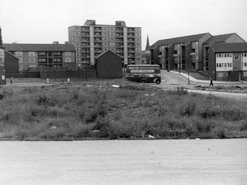 Burmantofts Street where the bus can be seen, just about to pass the junction with Rigton Approach. At the left edge properties in Argyle Avenue are visible. Land in the foreground would have once been the site of Argyle Road and Argyle Street. In the background the spire of All Saints Church in Richmond Hill is visible.