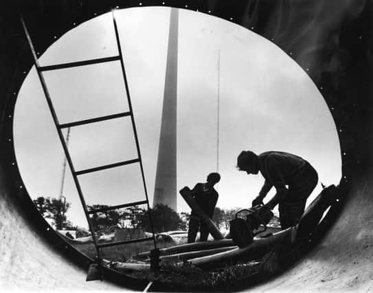 The new TV mast at Emley Moor, near Huddersfield, soars up through low cloud in September 1970 as John Orton and Derek Miller, framed in the broken section of the old mast start work on cutting up copper and aluminium cable.  Work on clearing the wreckage of the old mast, which was brought down by snow and ice 18 months ago was delayed while the committee of inquiry completed investigations.