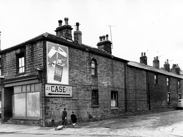 The junction of Town Street on the left and the empty shop front number 29. On the right is Grangefield Road where an advertisement hoarding promotes Cadbury's Dairy Milk Chocolate. A sign underneath gives directions to the J.I. Case Co Ltd. Two boys enter the street dragging a home made kart. Pictured in September 1963.