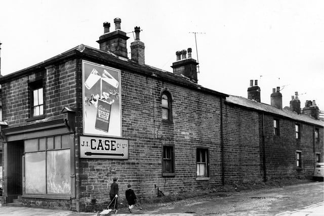 The junction of Town Street on the left and the empty shop front number 29. On the right is Grangefield Road where an advertisement hoarding promotes Cadbury's Dairy Milk Chocolate. A sign underneath gives directions to the J.I. Case Co Ltd. Two boys enter the street dragging a home made kart. Pictured in September 1963.