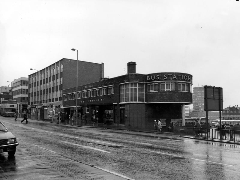 Buses can be seen in the picture as well as several people, some with umbrellas in this photo from October 1980.