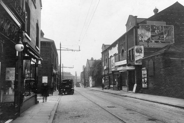 Town Street in June 1931. On the left, part of display window for Maypole dairy number 192 which has a white lamp outside. Next number 190 premises of Miss Hilda Baltye, ironmonger. Entrance to Spring Street can be seen. In the road a Co-op bakery delivery vehicle is parked outside store. On the right is the Lido Cinema. Built in 1912 as the Palace. In 1929 talking pictures arrived, the cinema was refitted and the name was changed to the Lido. In this photograph, Ken Maynard is starring in 'Sons of the Saddle'. On the gable end, a poster advertises 'Outside the Law' starring Mary Nolan. To the right of the cinema, a notice board gives details of shopping facilities in Bramley, the board shaped like a gothic window is advertising Leeds Permanent Building Society.