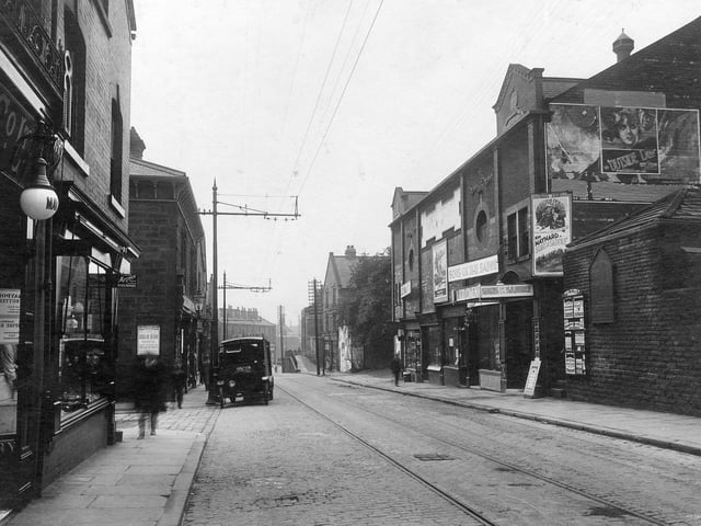 Town Street in June 1931. On the left, part of display window for Maypole dairy number 192 which has a white lamp outside. Next number 190 premises of Miss Hilda Baltye, ironmonger. Entrance to Spring Street can be seen. In the road a Co-op bakery delivery vehicle is parked outside store. On the right is the Lido Cinema. Built in 1912 as the Palace. In 1929 talking pictures arrived, the cinema was refitted and the name was changed to the Lido. In this photograph, Ken Maynard is starring in 'Sons of the Saddle'. On the gable end, a poster advertises 'Outside the Law' starring Mary Nolan. To the right of the cinema, a notice board gives details of shopping facilities in Bramley, the board shaped like a gothic window is advertising Leeds Permanent Building Society.