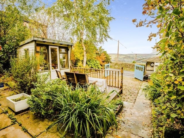 The rear of the property with a driveway, seating area and summer house - and beautiful scenery.