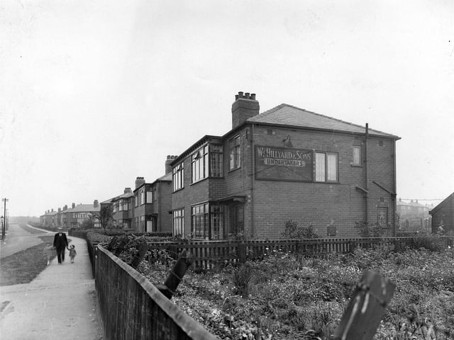 St. Alban Road looking north-west away from York Road in the direction of Harehills. The junction with Brander Road is visible between the houses about half-way along. At the near end of the row of semi-detached houses is no. 49, William Hillyard & Sons, undertakers. A man and two young children can be seen walking along the causeway. Pictured in August 1939.