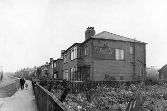St. Alban Road looking north-west away from York Road in the direction of Harehills. The junction with Brander Road is visible between the houses about half-way along. At the near end of the row of semi-detached houses is no. 49, William Hillyard & Sons, undertakers. A man and two young children can be seen walking along the causeway. Pictured in August 1939.