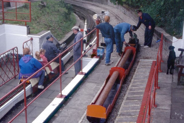 People can be seen riding behind the locomotives. Maintenance work is also being carried out.