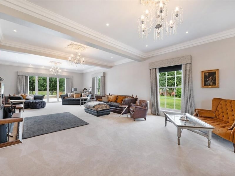 Double doors lead to the 36ft drawing room, which boasts an imposing stone fireplace with an open fire and wrought-iron club fender seating.