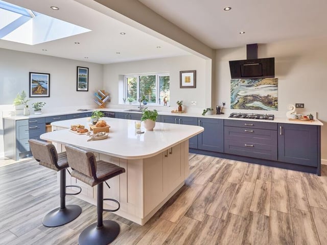 The kitchen is set around an expansive island and features classic shaker style two tone cabinetry, shelving and cupboards that wrap around the room, and quartz worktops.