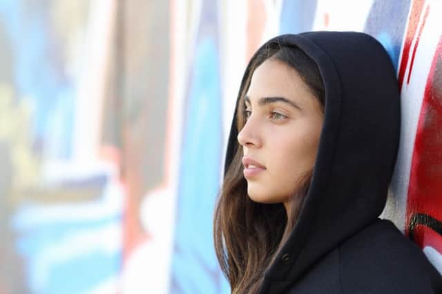 Profile portrait of a skater style teenager girl with an unfocused graffiti wall in the background