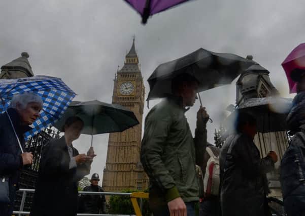 People shelter under umbrellas outside the Houses of Parliament as heavy rain falls in central London on the last day of spring. Image: Anthony Devlin/PA Wire