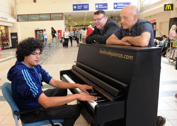 Nick Mitchell playing the new piano at Leeds City Station as station manager Sean Pearce and Melvyn Besbrode, who donated it, look on.