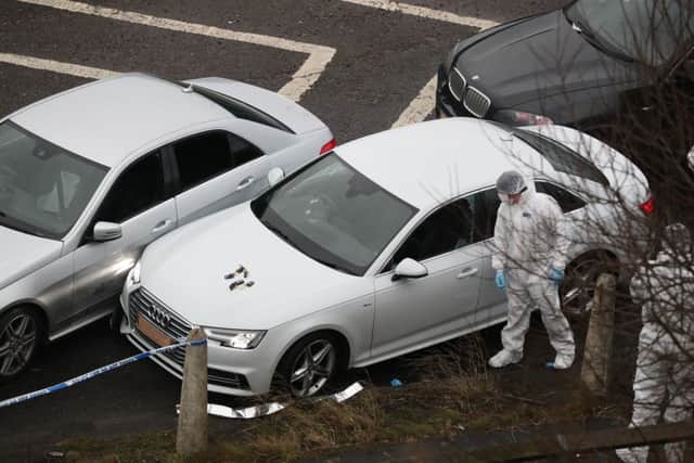 Police forensics officers examine a silver Audi with bullet holes in its windscreen at the scene near junction J24 of the M62 in Huddersfield